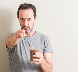 Senior man drinking chocolate milk shake pointing with finger to the camera and to you, hand sign, positive and confident gesture from the front