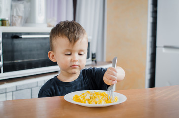 the child greedily in the kitchen eating an omelet in the afternoon in the summer