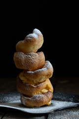 Slide of Yorkshire puddings on black plate with powdered sugar on black natural wooden background.