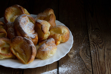 Yorkshire puddings with sugar powder on a white plate on a wooden table. Rustic style. Copy Space.