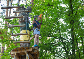 Naklejka na ściany i meble cute sporty 10 year boy is doing activity in adventure rope park with all climbing equipment like helmet, rope and carabiner. summer camp, active lifestyle concept