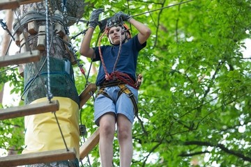 cute sporty 10 year boy is doing activity in adventure rope park with all climbing equipment like helmet, rope and carabiner. summer camp, active lifestyle concept