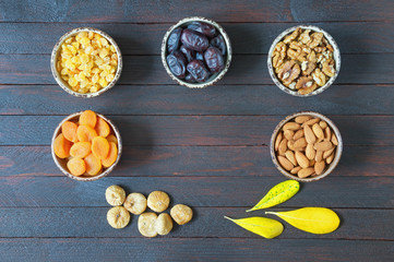 Various nuts and dried fruits (walnuts, almonds,  dried apricots, raisins, date fruits, figs ) on dark wooden background. Flat lay, free space for text