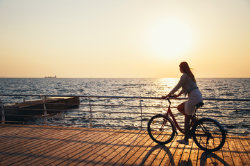 Obraz na płótnie Canvas Young woman cycling at the beach at sunrise sky at wooden deck summer time