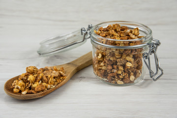 Jar full of granola and a woow spoon full of granola on the white wood table