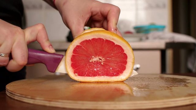 Woman's hands cutting fresh grapefruit on kitchen. Girl cutting orange with knife. Healthy lifestyle concept. Slow motion. Close-up.