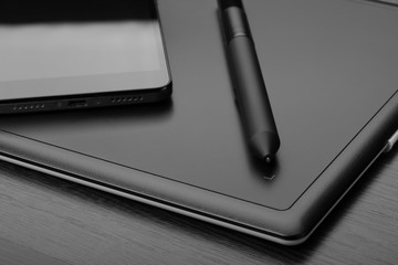 Graphic tablet with stylus and smartphone on a wooden table