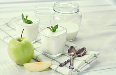 Two glass jars of homemade yogurt with mint and apples on a light textile background. One empty jar of yogurt and jar of leaven.