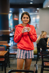 A happy youthful Indian lady smiling and enjoying a coffee in a cafe