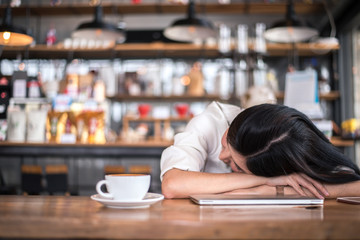 Asian woman is resting and sleeping in a coffee shop because she is tired of working all night. Business owner and freelance concept. Healthcare and Relaxation theme.
