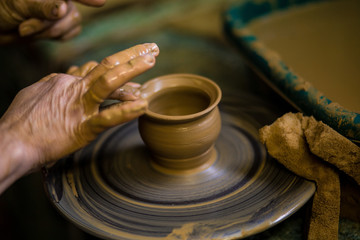 Fototapeta na wymiar Close-up hands of potter in apron making vase from clay, selective focus. Making it together. Top view of potter teaching to make ceramic pot on pottery wheel