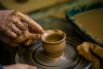 Fototapeta na wymiar Close-up hands of potter in apron making vase from clay, selective focus. Making it together. Top view of potter teaching to make ceramic pot on pottery wheel