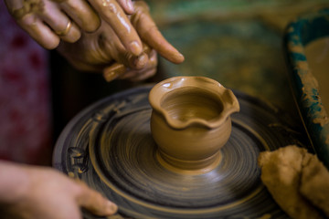Close-up hands of potter in apron making vase from clay, selective focus. Making it together. Top view of potter teaching to make ceramic pot on pottery wheel