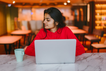 Happy young attractive Indian student working at a laptop