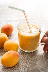Apricots and smoothie in glass on linen tablecloth and woman's hand taking a glass.
