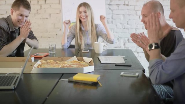 Young creative coworkers have a meal together. Business team are eating pizza in the office. Woman brings a box of pizza to office workers and they are happy