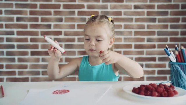 Small little girl draws picture at the table and eating raspberry. Very smooth dolly shot 4K video.