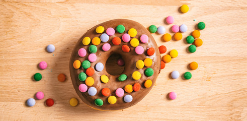 Donut chocolate glaze and sprinkles, top view and isolated, wooden table background.