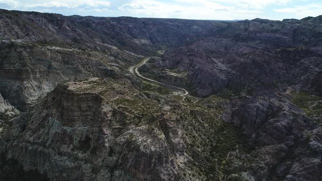 Aerial drone scene of Atuel river canyon in San Rafael, Mendoza, Cuyo Argentina. Camera moving upwards. Gravel street next to the willows trees and river. Colorfull rocks.