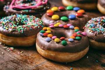 Donuts chocolate glaze and sprinkles, wooden table blurry background.