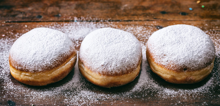  Krapfen with powder sugar, three and isolated on wooden background.