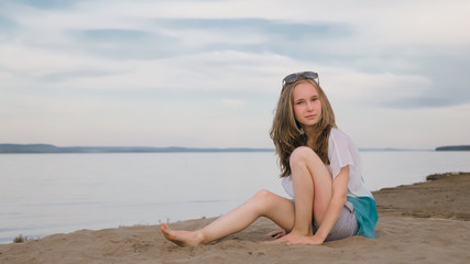 One beautiful teenage girl with brown hair outside on a beautiful summer day. The woman is sitting on the beach. The sun was gone in the sunset.