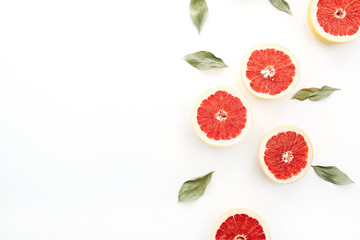 Sliced grapefruits and green leaves on white background.