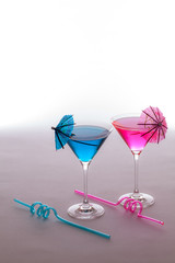Fun vacation party drinks. Pink and blue cocktails glasses with curly straws and umbrella decorations