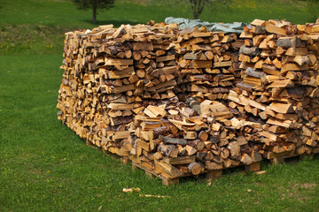Pile of stacked firewood on green grass lawn.
