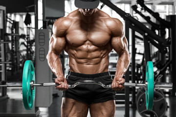 Fototapeta na wymiar Muscular man working out in gym doing exercises with barbell for biceps, strong male naked torso abs