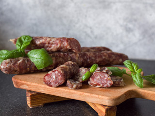 Dry homemade sausage on a wooden background decorated with a green basil on a gray background. Soft focus.