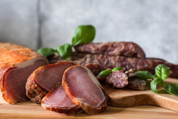 Dry home-made sausages and meat, serving slices on a wooden background decorated with a green basil on a gray background. Soft focus.