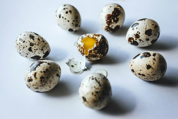 Broken quail egg surrounded by whole eggs on white background, close up. Concept killing, ritual, suicide, sacrifice