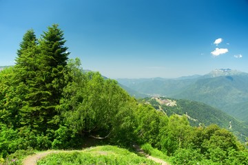 Mountain tourism. Green slope of the high big mountains. Alpine meadows in the Caucasus Mountains. Flowers and grasses. Beautiful blue sky and clouds.