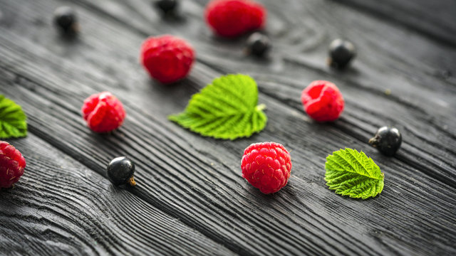 .raspberries and currants on a black wooden background