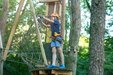 cute sporty 10 year boy is doing activity in adventure rope park with all climbing equipment like helmet, rope and carabiner. summer camp, active lifestyle concept