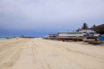 Fototapeta na wymiar Industrial area on Dhangethi Island, Maldives. Sand road, old boats on blue sky background.