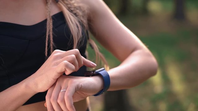 Unrecognizable young caucasian woman with long braided fair hair wearing black sportswear using her fitness tracker before outdoors workout. Handheld slow motion medium shot