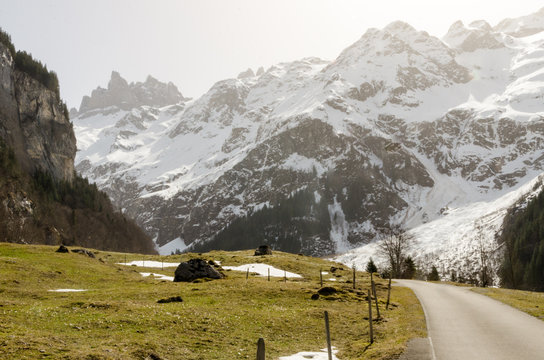 Mountain road towards the apline snowy peaks on sunny afternoon