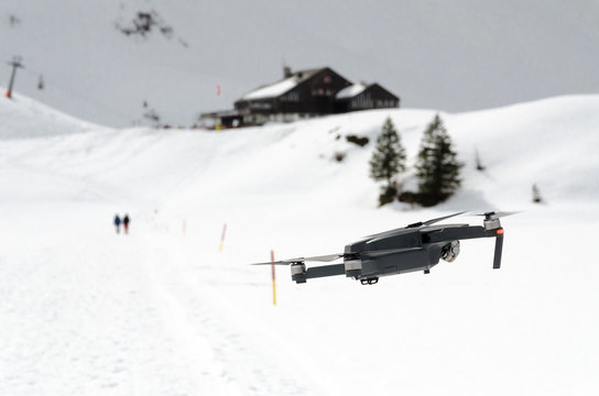 A camera drone hovering and flying over snowy skiing hills in alps