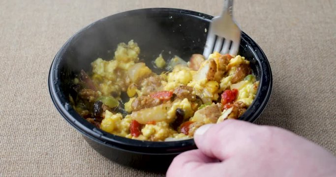 Video of a microwaved scrambled egg burrito meal TV dinner in a black tray being stirred with a fork.