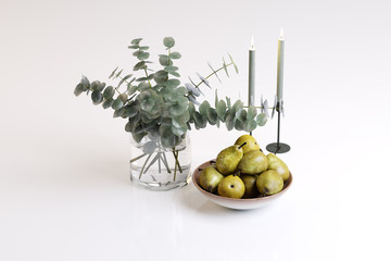 Composition of a plant of a vase, candles and a pear in a plate
