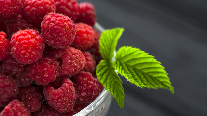 Raspberry berries in a glass plate on a black background.