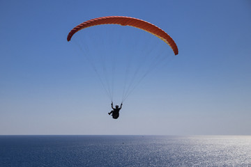 Flight on a red paraglider over the sea. A brave man is flying on a paraglider over the open sea on...