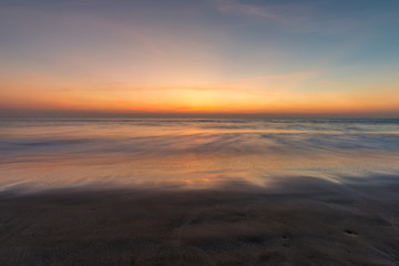 Fototapeta na wymiar Blurred waves on the beach, sunset cloudy sky.