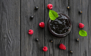 jam and raspberries and currants on a wooden background