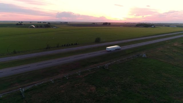 Semi Truck driving on freeway into the distance during sunset from aerial view.