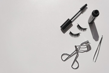 Black false lashes strips, mascara, tweezers, curler on white  background