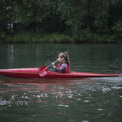 young teenager girl actively manages a sports kayak boat on a beautiful river.