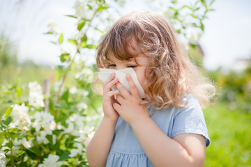 Allergy concept. Little girl is blowing her nose near blooming tree.